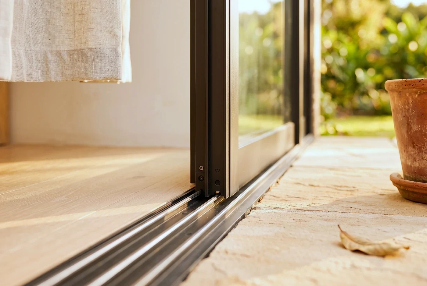 Close on the meeting stile and flush floor track of a sliding door, the room soft behind
