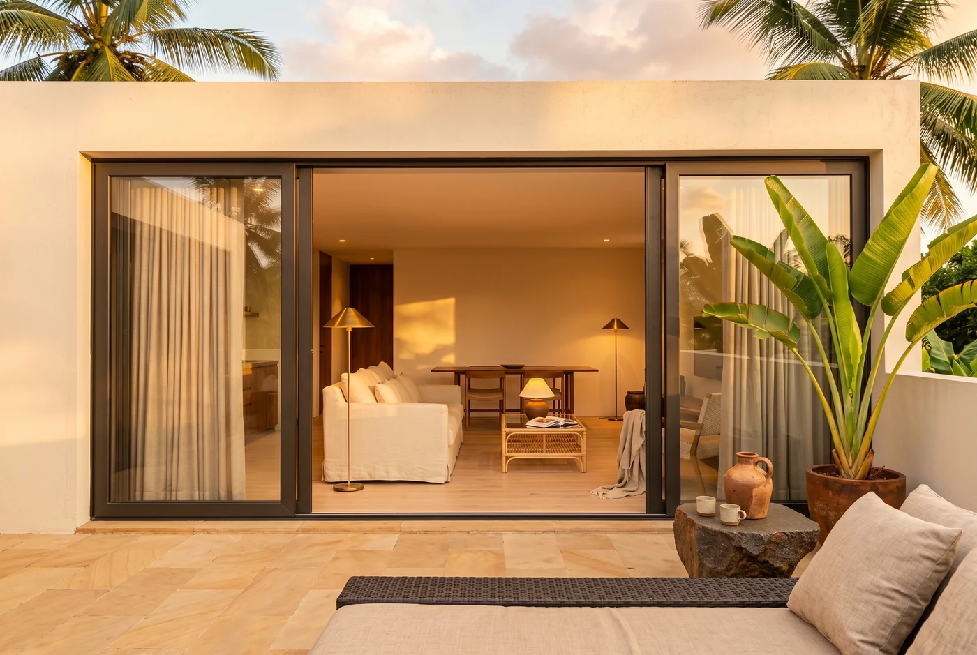 Looking back in from a terrace at golden hour through open sliding doors, lamps lit inside